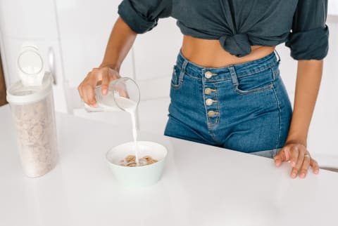 Anonymous female in casual outfit pouring fresh milk into bowl with cereal corn flakes while preparing healthy breakfast at home Anonymous female in casual outfit pouring fresh milk into bowl with cereal corn flakes while preparing healthy breakfast at home