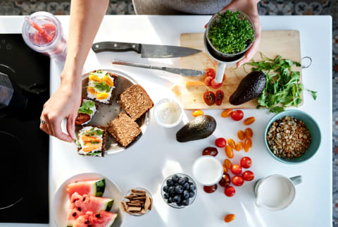 Overhead of woman cooking and preparing healthy meal with fresh avocado, veggies, watermelon, blueberries, and other fruit in kitchen Overhead of woman cooking and preparing healthy meal with fresh avocado, veggies, watermelon, blueberries, and other fruit in kitchen