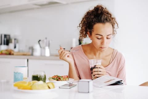 woman eating breakfast and reading in kitchen woman eating breakfast and reading in kitchen